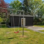 Schwarzes Gartenhaus mit Spielgerüst und Rutsche im grünen Garten.