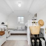 Schlafzimmer mit Doppelbett, Nachttisch und Kleiderschrank. Wandgestell mit Strohhut und Tasche.