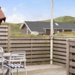 Terrasse mit Tisch und Stühlen, Holzzaun, Blick auf grüne Hügel und Haus im Hintergrund.