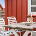 Holztisch mit Stühlen vor rotem Haus mit Flasche und Schalen.