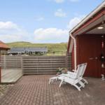 Terrasse mit weißen Liegestühlen, rotem Holzhaus und Blick auf grüne Dünen.