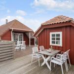 Rote Holzhäuser mit Terrasse und Tisch. Weiße Stühle und Holzdecke.