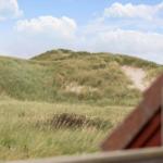 Grüne Dünen unter blauem Himmel, Blick von einem Haus mit rotem Dach.