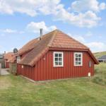 Rotes Holzhaus mit Schieferdach und weißen Fenstern in grüner Umgebung.