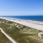 Strand mit Dünen und Windkraftanlagen im Hintergrund.