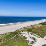 Strand mit Dünen und blauem Meer unter klarem Himmel.