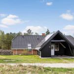 Haus mit dunklem Holz und Ziegelfassade, umgeben von Gras und Bäumen unter blauem Himmel.