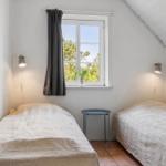 Zwei Betten, ein Fenster mit Blick auf Bäume, Wandlampen und ein kleiner Tisch.