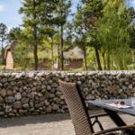 Terrasse mit Tisch und Stühlen. Steinmauer und Wald im Hintergrund.