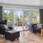 Wohnzimmer mit Ledersofa, Sessel und Terrasse mit Blick auf Wald.