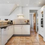 Küche mit weißen Schränken, dunkler Arbeitsplatte und Terrakottafußboden.