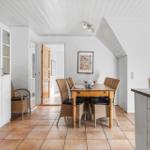 Esszimmer mit Holztisch, Stühlen und Küchenzeile. Weiße Wände und Holzdecke.