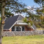 Haus mit Steinmauer und großen Fenstern, umgeben von Bäumen.