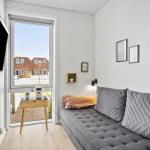 Ein Raum mit grasem Sofa, Fernseher und Fensterblick auf Häuser.