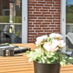 Terrasse mit Holztisch, Stühlen und Blumenarrangement vor Backsteinmauer.