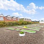 Minigolfplatz mit mehreren Bahnen vor Reihenhäusern auf Kiesgrund.