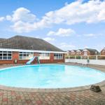 Runder Pool mit Rutsche und Terrasse vor einem Gebäude.