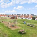 Grüner Spielplatz mit Schaukel und Tisch vor Reihenhäusern.