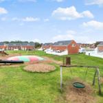 Grüner Spielplatz mit Schaukel und Klettergerüst vor roten Häusern.