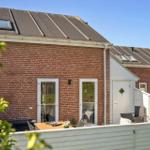 Roter Backsteinbau mit Terrasse und Gartentisch. Weiße Tür und Dachfenster sichtbar.