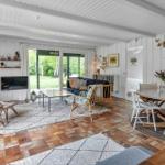 Wohn- und Essbereich mit Kamin, TV und Terrassentür. Holzboden und weiße Wände.