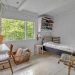 Zimmer mit Bett, Schreibtisch, Stuhl und Fenster mit Blick auf Bäume.