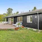 Schwarze Holzhütte mit Terrasse und Garten. Weiße Möbel und Pflanzen.