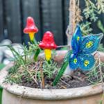 Terrassenkübel mit Glasfiguren: zwei Pilze und ein Schmetterling.