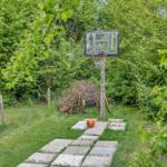 Basketballkorb im Garten mit Kletterpfad und Ball auf Steinplatten
