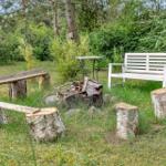 Außenbereich mit Holzbank, weiße Bank und Feuerstelle im Gras.