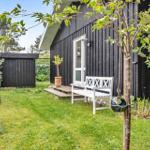 Hinterhof mit weißer Bank, Grasfläche und Baum vor schwarzem Holzhaus.