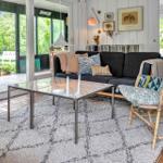 Ein Wohnzimmer mit Sofa, Stuhl und Tisch. Durchgänge führen zu einer Terrasse mit Garten.