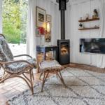 Wohnzimmer mit Stuhl, Kamin und Fernseher. Große Fenster mit Blick auf Garten.