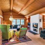 Wohnzimmer mit Holzdecke, Kamin und grünen Sesseln.