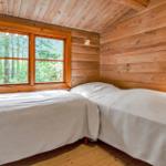 Zwei Betten in einem Holzhauszimmer mit Fensterblick auf Wald.