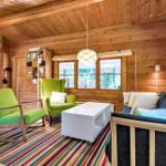 Wohnzimmer mit Holzwand, grünen Sesseln, Sofa und buntem Teppich.