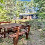 Holztisch mit Bänken im Wald. Im Hintergrund ein Holzhaus mit Dachboden.