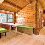 Holzhaus mit Essbereich, grüner Sitzbank und Fenster zum Wald.