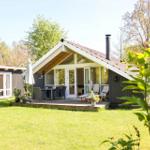 Haus mit Terrasse, Garten und Grillplatz. Holzhaus mit Schornstein und großen Fenstern.
