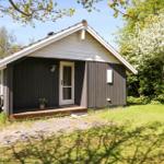 Holzhaus mit weißem Dach und Eingangstür. Grün umgeben mit blühendem Baum.