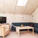 Wohnzimmer mit Holzwand, Sofa, Sessel und Fernseher unter Dachschräge.