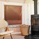 Raum mit Holzwand, Bett, Stuhl und Kaminofen.