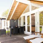 Terrasse mit Tisch, Stühlen und Liegestühlen unter Holzdecke. Glastüren führen ins Haus.