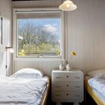 Zwei Betten mit weißer Bettwäsche stehen an einem Fenster mit Blick auf Bäume.