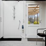 Helle Eingangshalle mit weißen Wänden, Tür und Garderobe. Außenterrasse mit Sitzgelegenheit sichtbar.