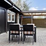 Terrasse mit Tisch und Stühlen vor schwarzem Haus mit Holzüberdachung.