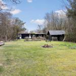 Schwarzes Haus mit Garten, Holzstapel und kleiner Hütte im Wald.