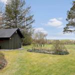 Ein grünes Holzhaus mit Garten, Tisch und Bäumen im Hintergrund.