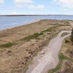 Grasland mit Steigweg und Strand. Blick auf Wasser und Horizont.