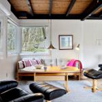 Wohnzimmer mit Sofa, zwei schwarzen Ledersessel und Holztisch unter Holzdecke.
